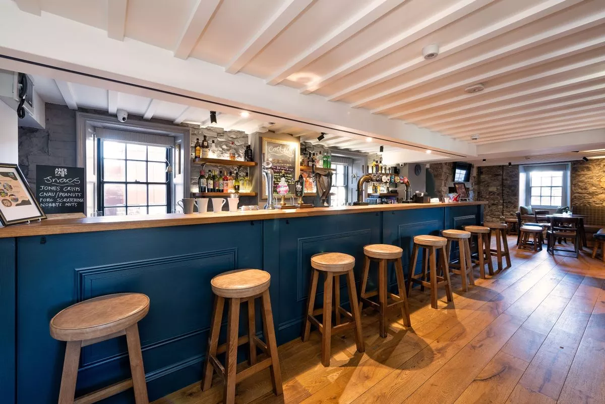 The new, substantial bar is a sociable space at The renovation, conversion and transformation of T'yn Llan commnity pub in Llandwrog, Gwynedd this is the new build extension with restaurant, catering kitchen, facilities and community room -  this is inside the old pub after renovation