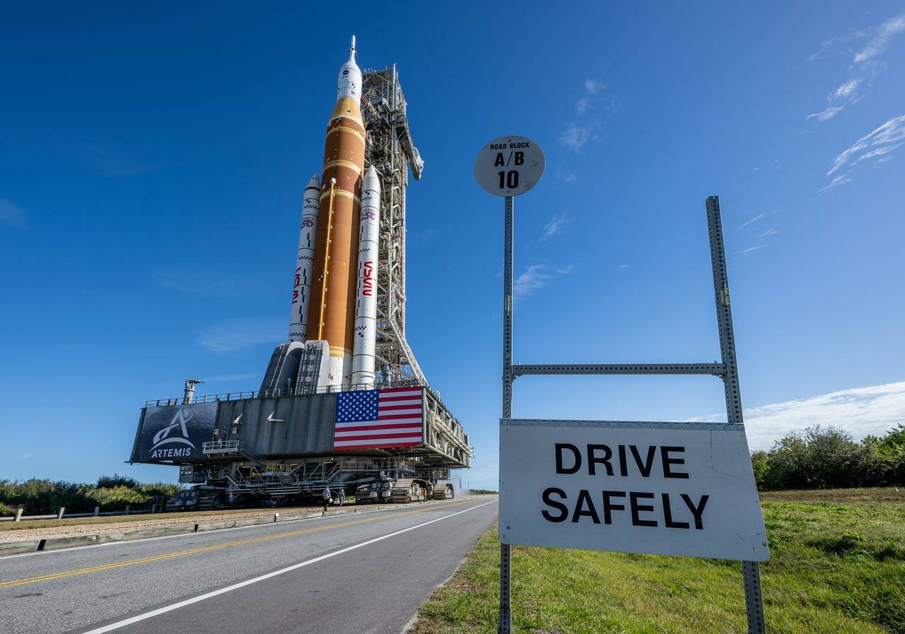 Artemis II SLS heading to the launch pad with "Drive Safely" sign in the foreground