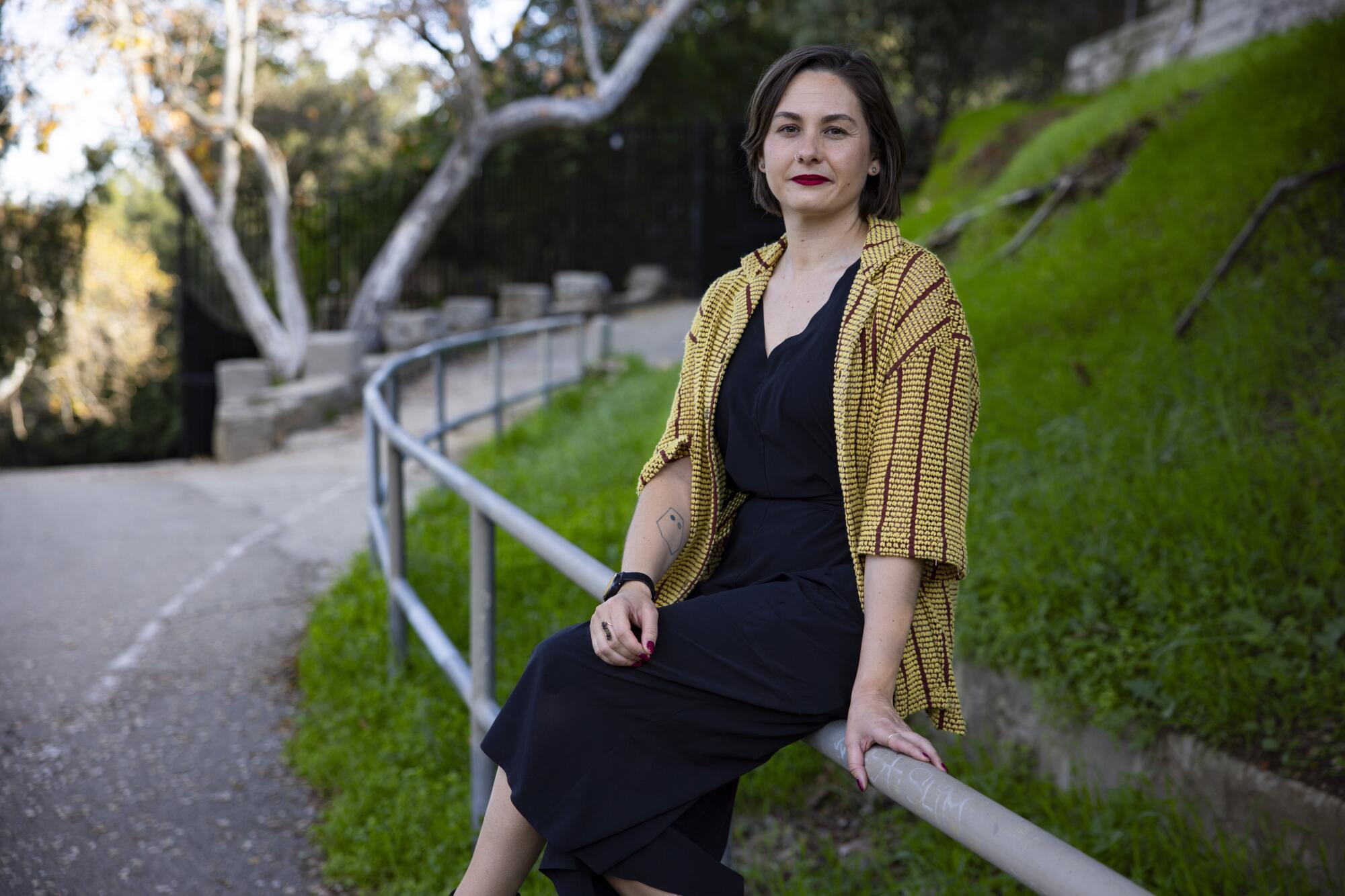 A woman in a black dress with a yellow jacket sits on a railing.