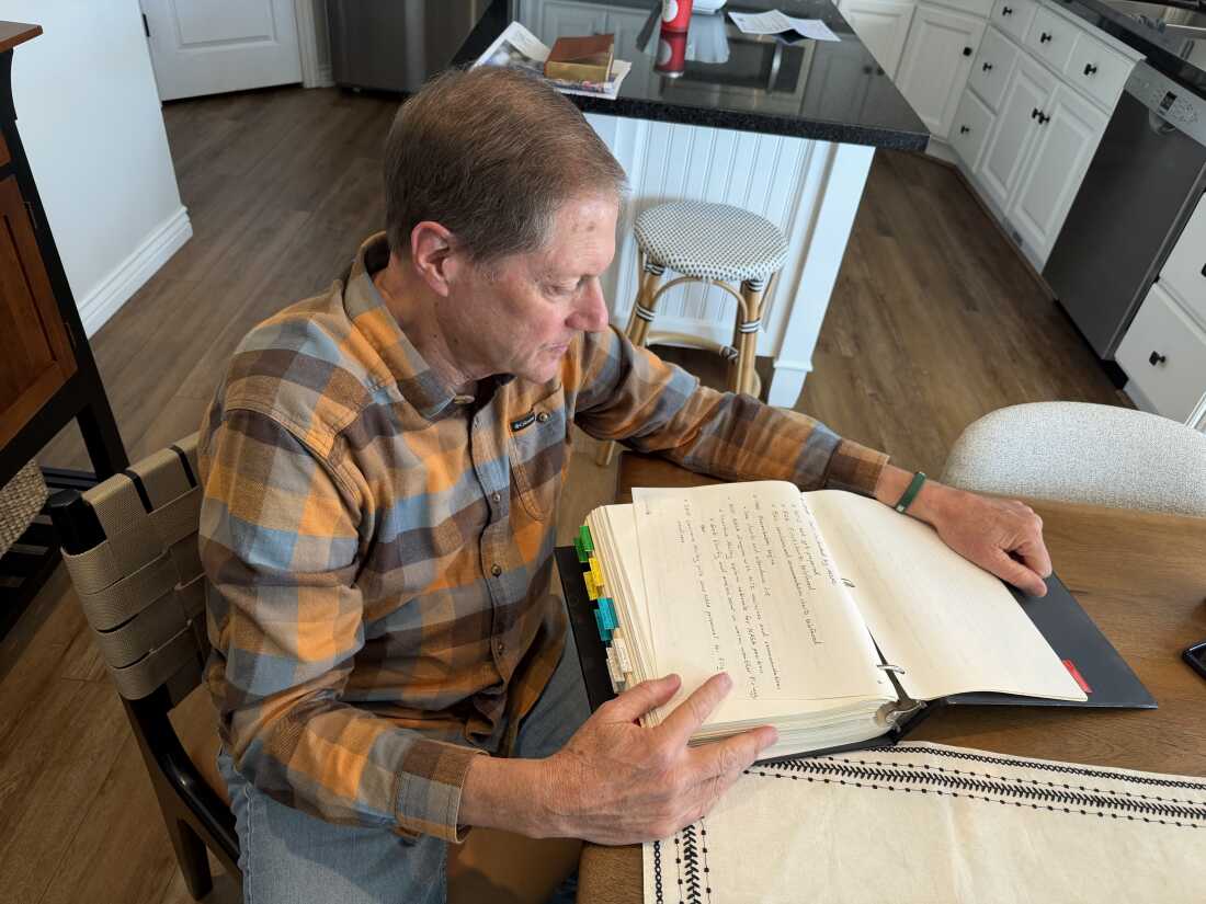 Seated at a kitchen table, Brian Russell looks at notes from the Challenger mission that are in a three-ring binder.