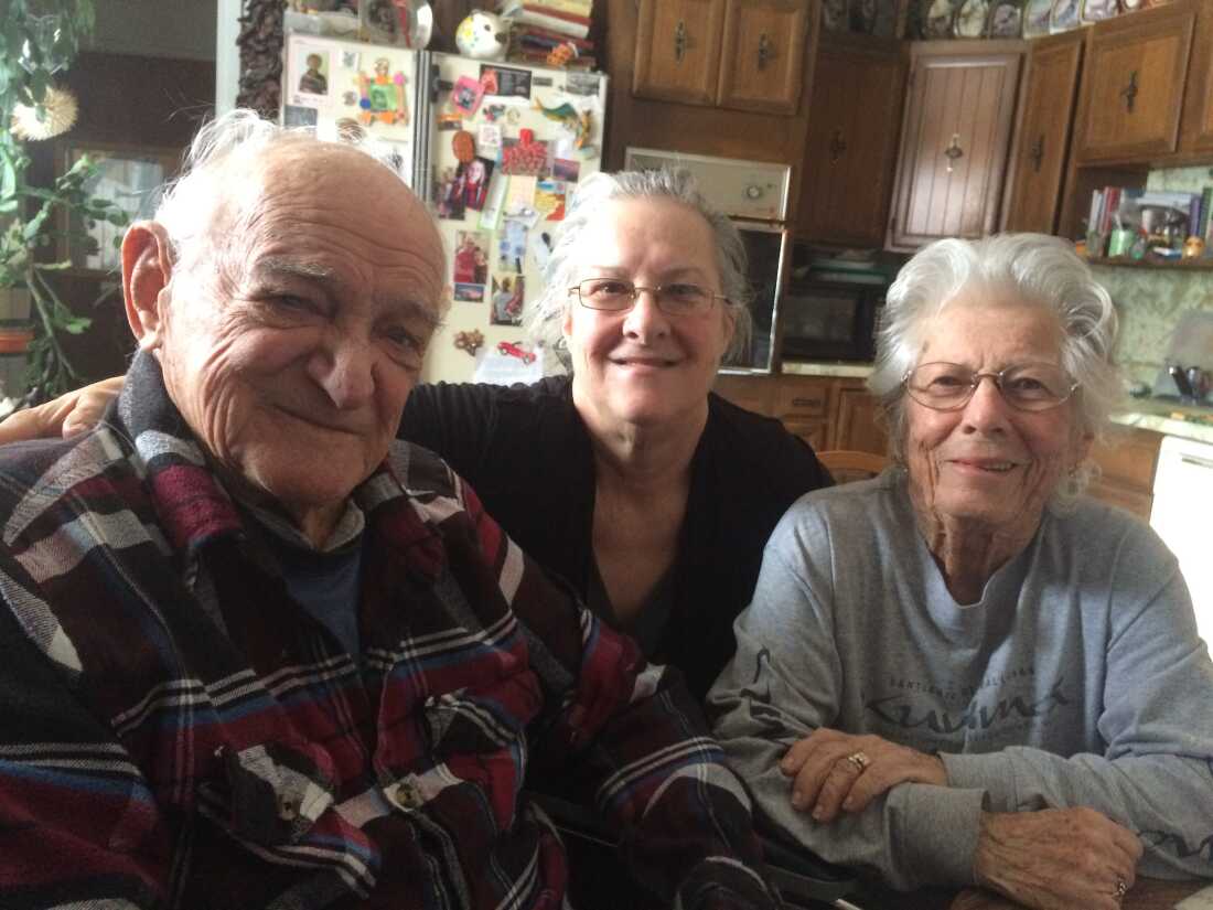 Seated in a kitchen with wooden cupboards and a fridge behind them are Bob Ebeling, his daughter Kathy (center) and his wife, Darlene, in 2016.