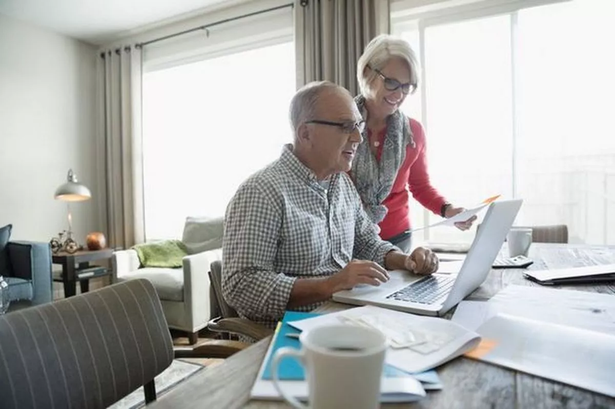 An elderly man and woman are working together on a computer 