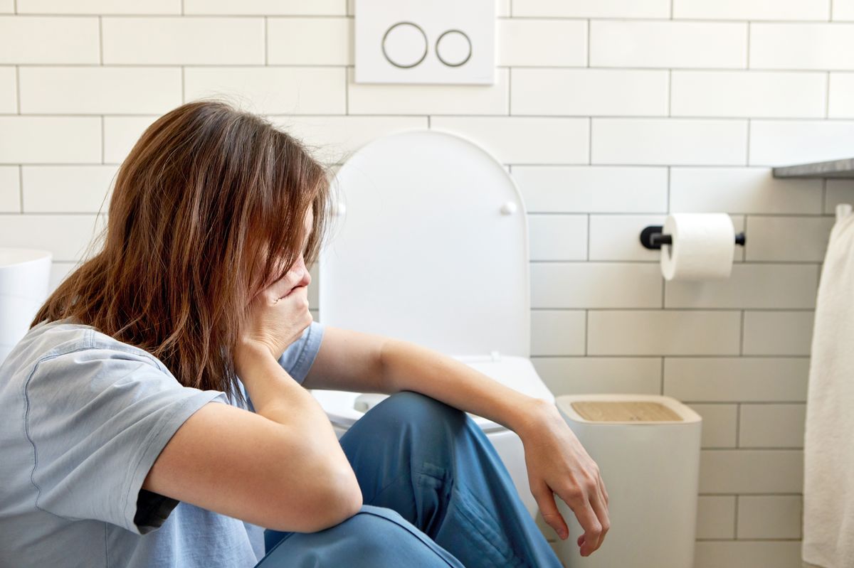 Young woman sitting on bathroom floor feeling nauseous,