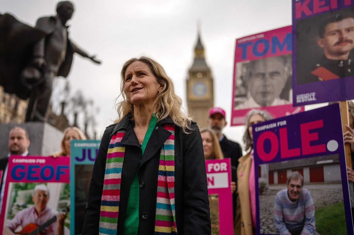 A woman stood in front of the Elizabeth Tower with campaigners and placards