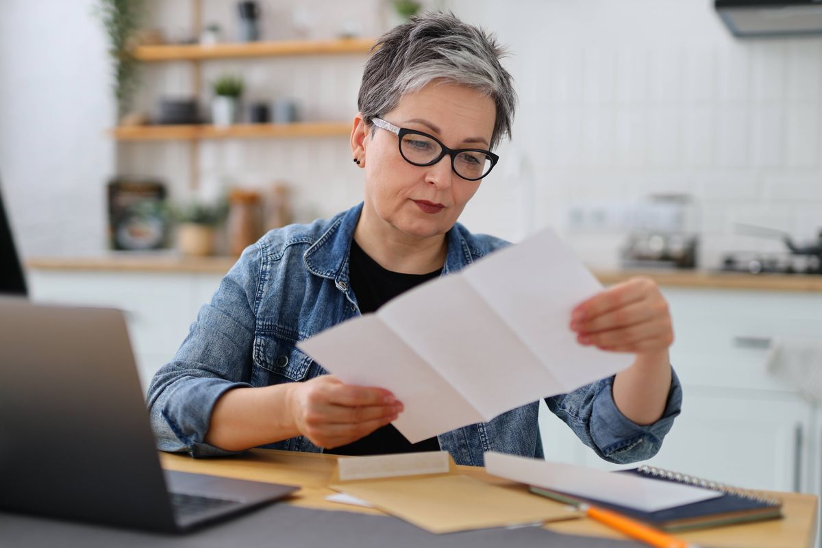 Serious mature woman in glasses reading the bill in the kitchen.