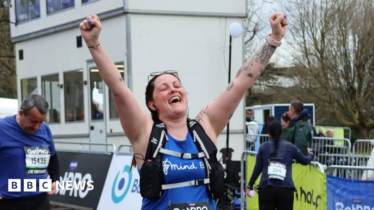 Alicia wearing a running bib and Bath Mind branded tank top with her hands in the air at the Bath Half Marathon finish line.