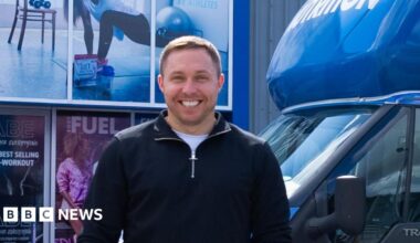 Tom Ryder, who is smiling at the camera, is standing in front of van with Applied Nutrition branding and holding an Applied Nutrition branded water bottle.