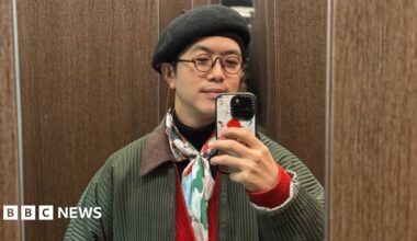 A man in a black beret and colourful scarf taking a photo in the mirror with his iPhone