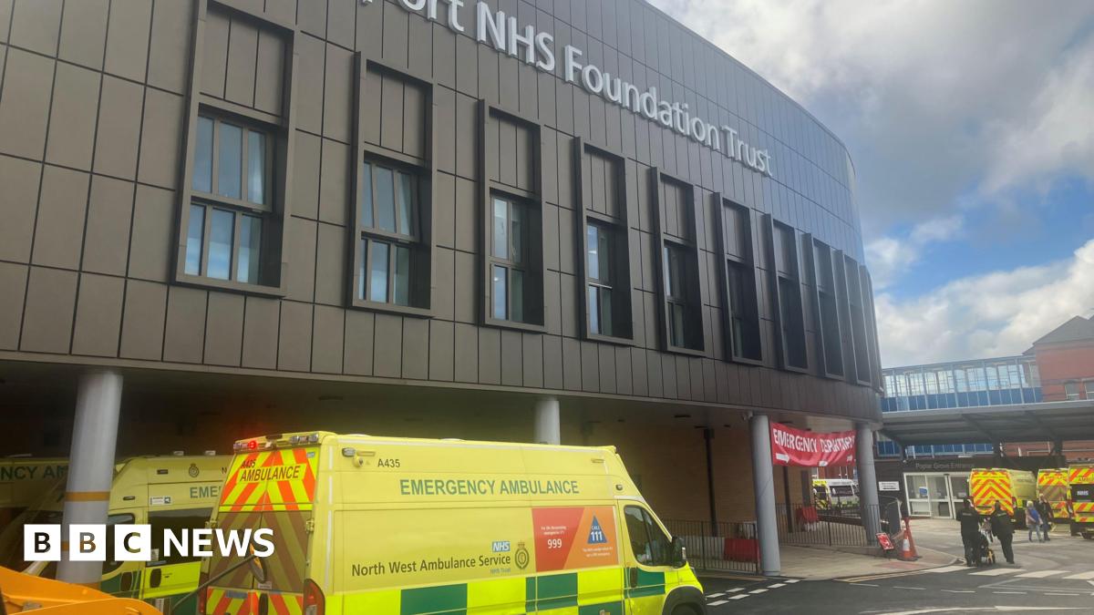 An ambulance at the entrance to Stepping Hill hospital in Stockport, with the main hospital building above a roadway and entrance signs and buildings.