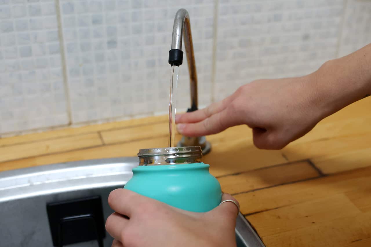 A close up of a person filling up a drink bottle with tap water