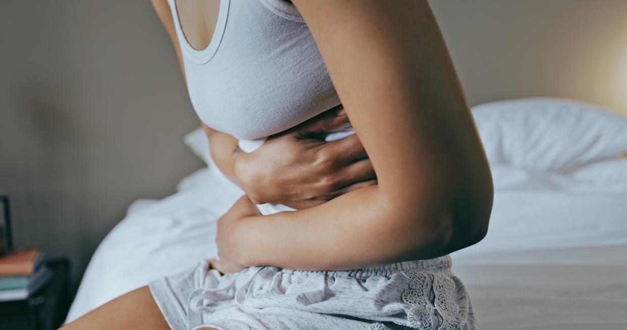 Close-up shot of a woman sitting on the edge of a bed holding her stomach in pain