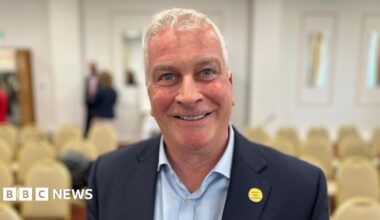 Deputy Andrew Niles - A man with white hair smiling at the camera. He has a blue suit on, with a blue shirt.
