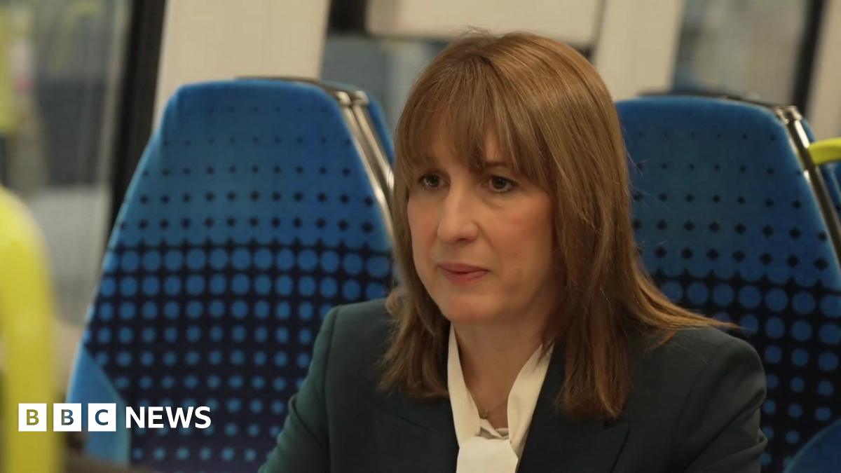 Rachel Reeves, a woman with shoulder length brown hair and brown eyes. She is wearing a cream blouse and navy suit jacket. She is being interviewed in a train carriage