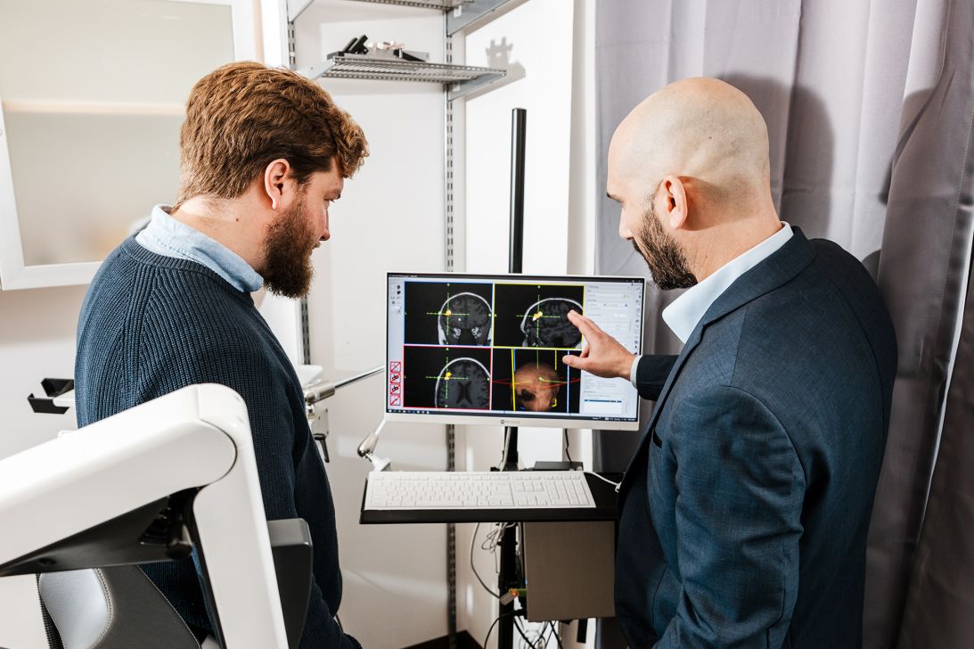 Dr. Christopher Austelle (left) and Dr. Ian Kratter examine Valerie Zeko's brain scans in a Brain Stimulation Lab treatment room.