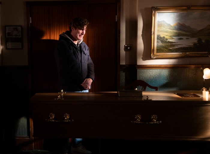 27_01_coro_theo_02 Theo stands over Billy's coffin in a darkened chapel of rest in a scene from Coronation Street