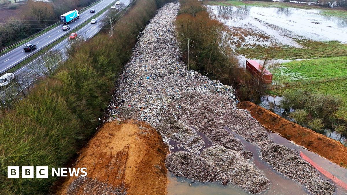 An aerial shot of the dumped waste, stretching out in a road-like line into the distance and surrounded on both sides by trees next to a motorway.