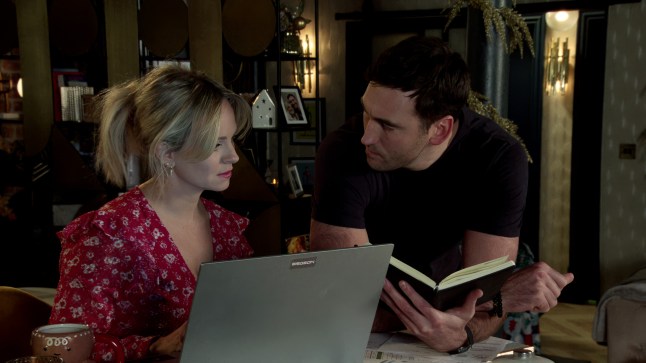 Kit and Sarah looking through a diary with a laptop open in front of them in Corrie