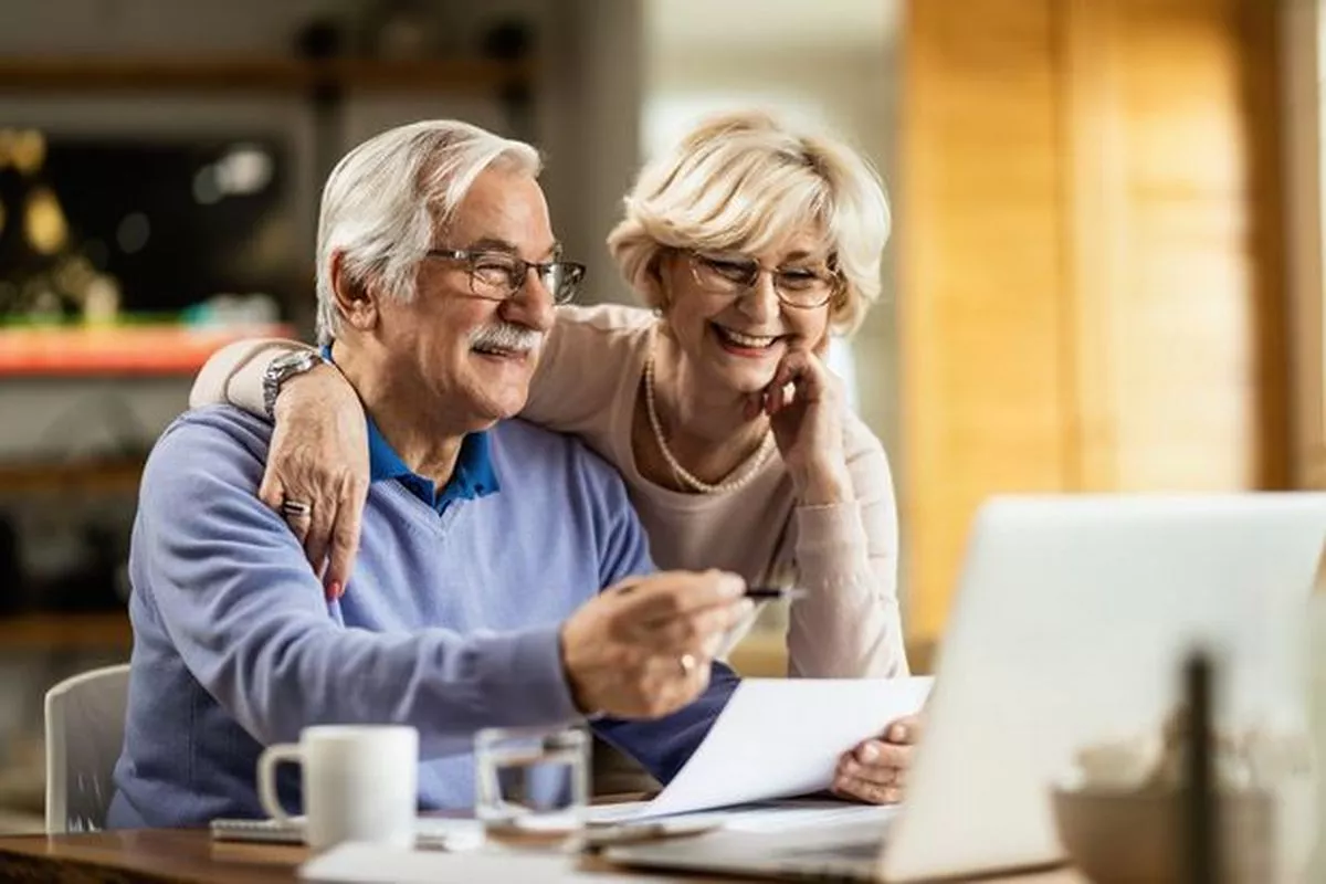 A man and woman are sitting looking at a computer screen smiling 