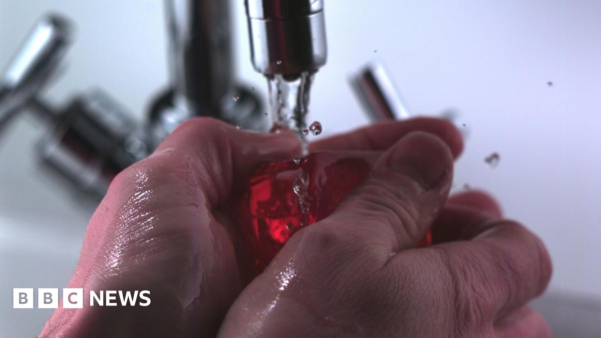 A pair of hands are underneath a tap of running water and are holding a bar of red soap. They are about to lather up the soap.