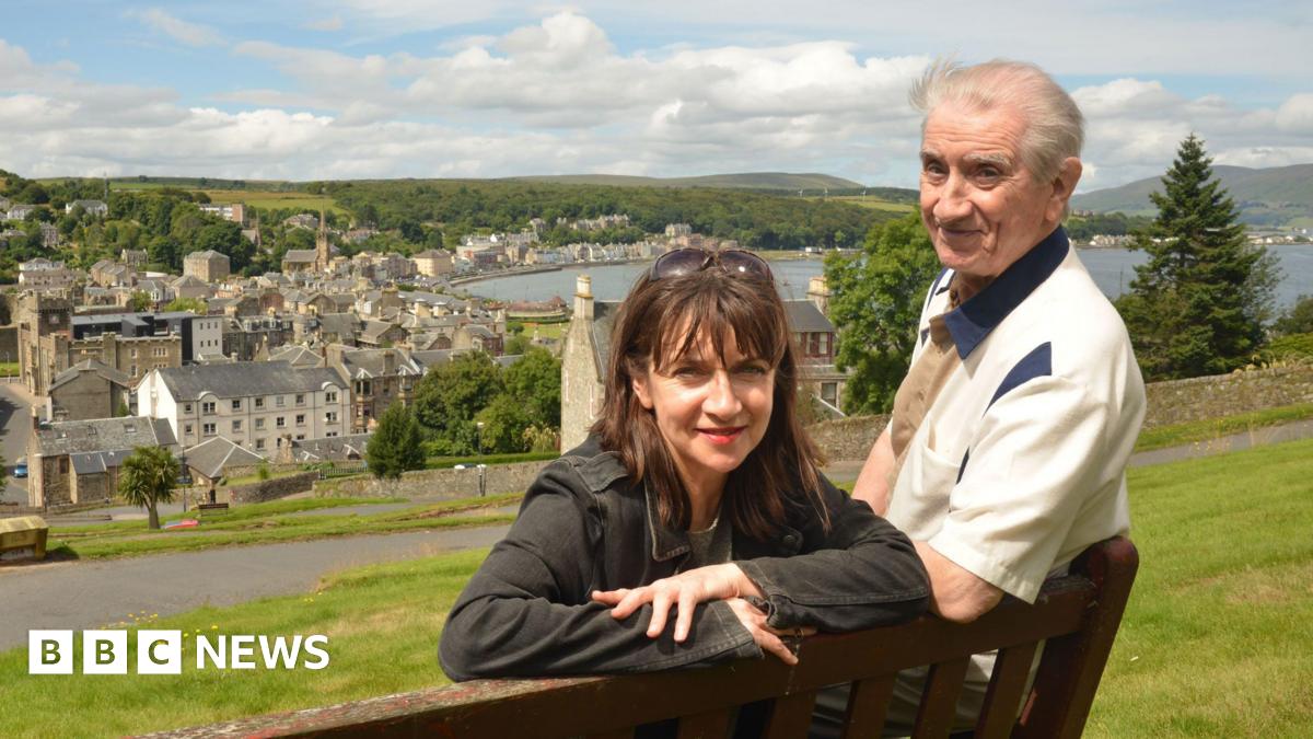 Maureen Beattie and her late father Johnny Beattie in an old photo leaning on a park bench in Rothesay, Isle of Bute. They are on top of a hill overlooking the town and the water below.