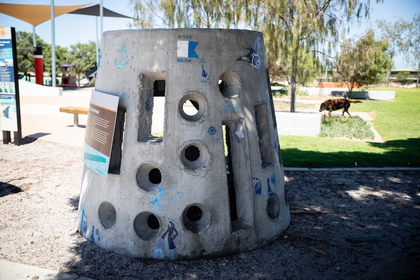 A cylindrical concrete structure with holes, atop some mulch.