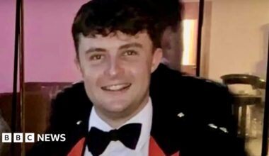 Captain Philip Gilbert Muldowney smiles as he looks into the camera, with short dark hair, wearing a dress suit and bow tie.
