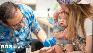 A one-year-old is held by his mother while he receives an MMR vaccine at a clinic in Texas
