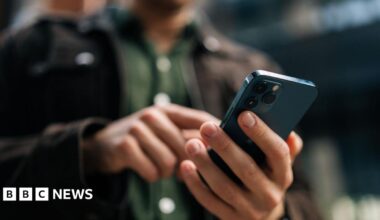 A man wearing dark clothes typing on a smartphone.