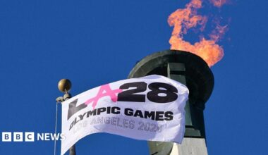 Prime Minister Mark Carney, wearing a black suit jacket, and a white button-up shirt leans his chin on his hands. He has short grey and black hair and is looking away from the camera.