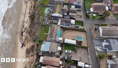 A drone shot above chalets and gardens along a cliff edge.