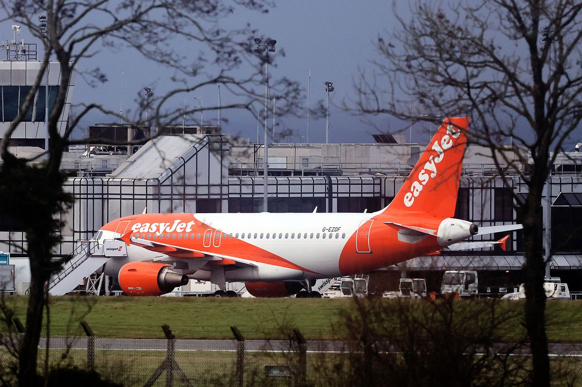 An easyJet plane parked on the runway Belfast International Airport with its door open and stairs attached, with terminal visible in background