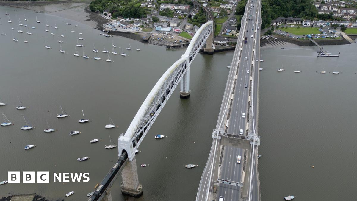 Bird's eye view of the Tamar bridge with toll booths at one end and several vehicles travelling along it.