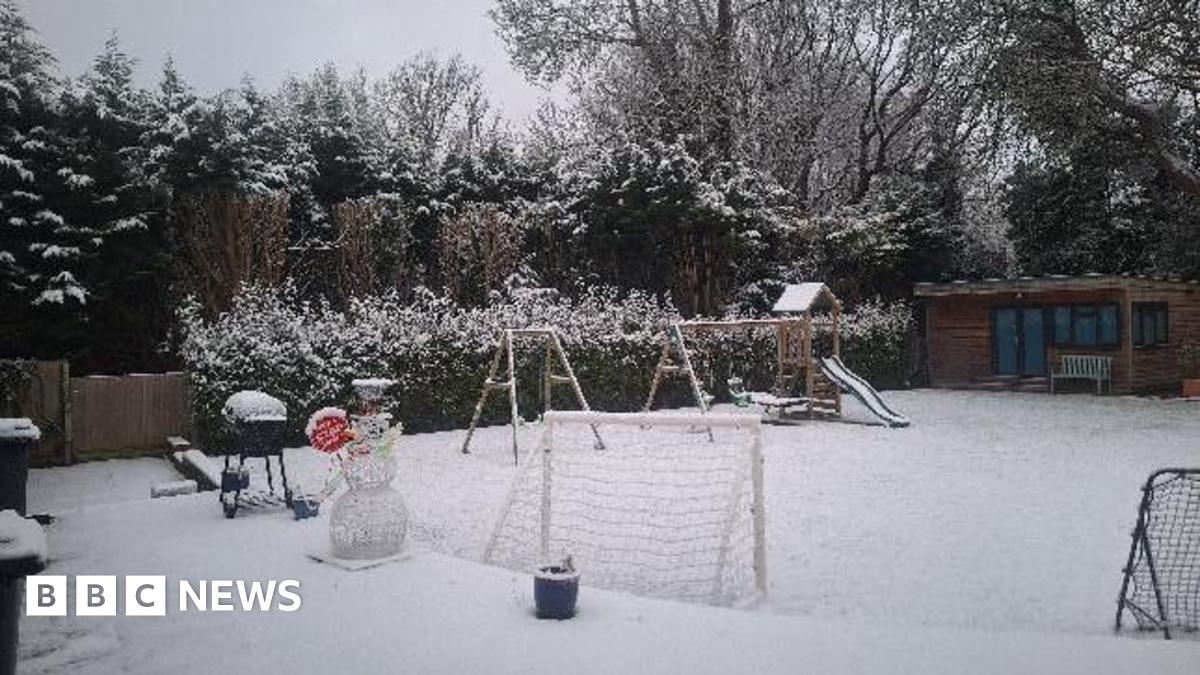 A "stop here santa" Christmas decoration covered in snow looks like a snowman in a garden. There is play equipment and everything is snowy.