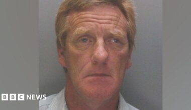 A police mugshot of Anthony Burns, 63, who has ginger hair and is wearing a light blue collared shirt. He is looking into the camera with a sorrowful expression.