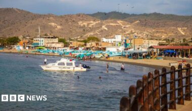 A boat can be seen bobbing in the water off the beach in Puerto López. Several people are swimming in the sea. Smaller boats are lying on the sand.