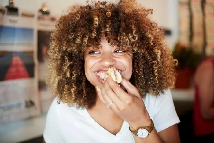 Person smiling while eating food; background includes blurred newspapers