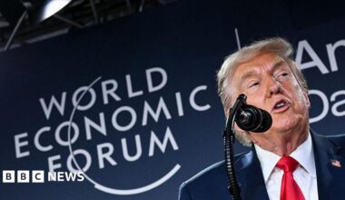 Close up shot of Donald Trump speaking into a microphone in front of a board with the words "World Economic Forum" on it.