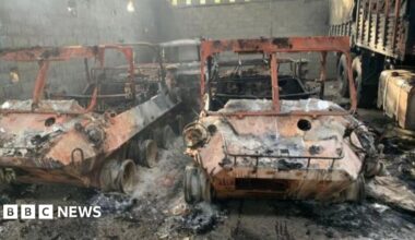 Maduro on the USS Iwo Jima, wearing a grey tracksuit and holding a bottle of water. He is blindfolded and wearing ear protection.