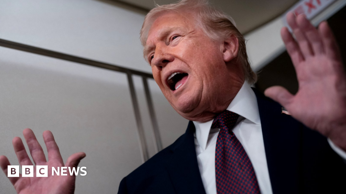 US President Donald Trump wearing a dark suit, white shirt and blue tie with red dots gestures with his hands as he speaks on Air Force One