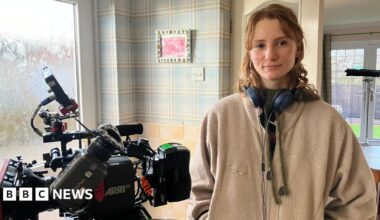 Sienna Rose, a woman with dark curly hair seen in a sepia-toned image with eyes closed, wearing large hoop earrings and singing into an old-fashioned microphone