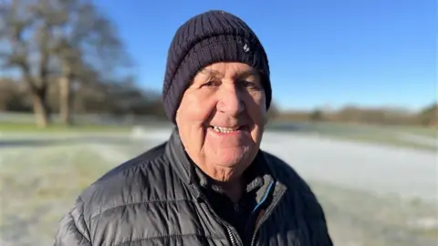 GEORGE CARDEN/BBC James Shelford wears a dark blue jacket and wooly hat as he smiles into the camera.