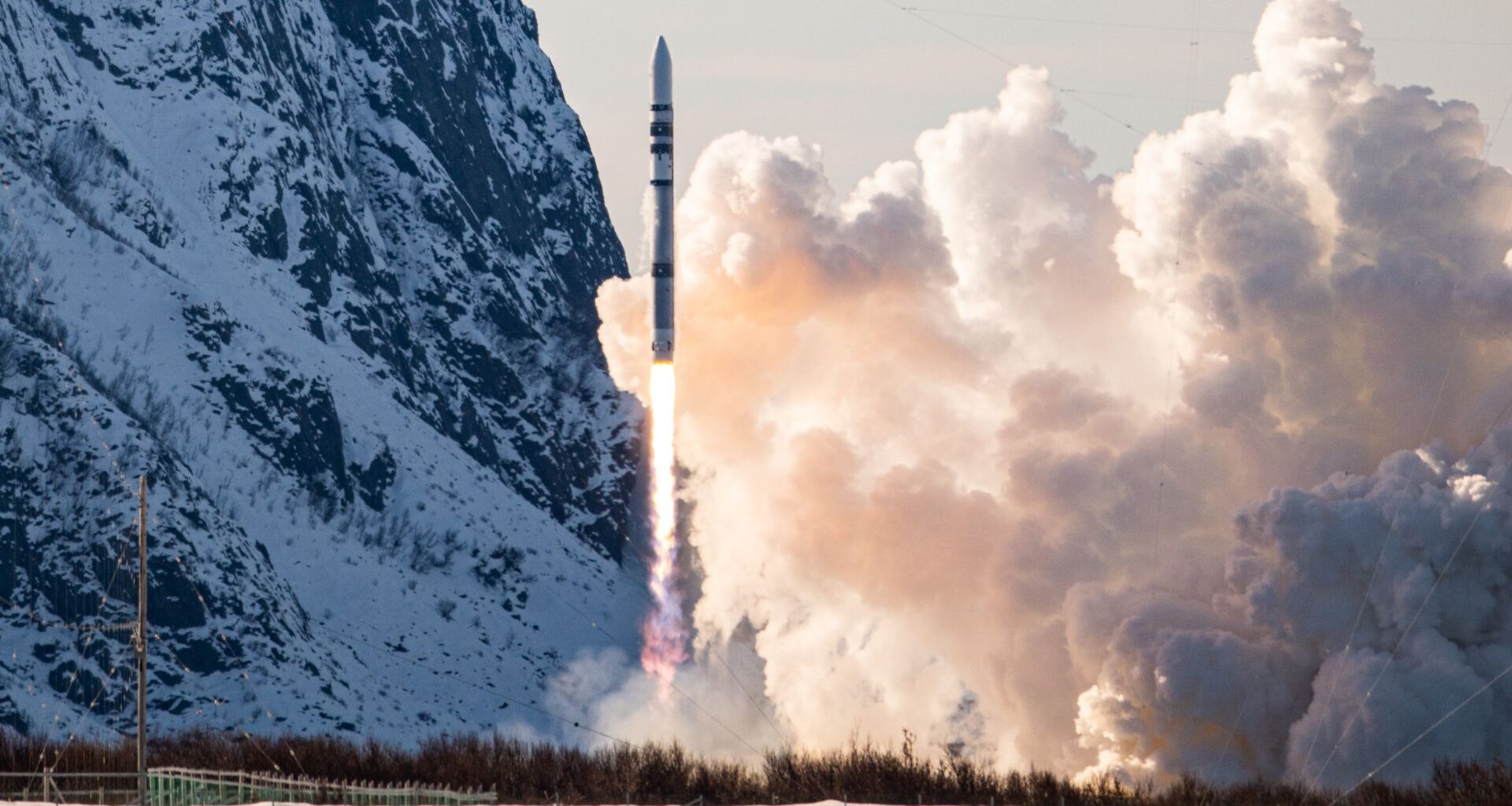 a black and white rocket launches with a snow-covered mountain in the background
