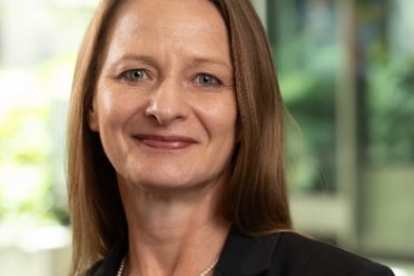 Woman with brown hair and black blazer smiles at camera 