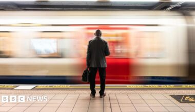 Senior passenger with laptop bag standing in front of speeding train on subway platform - stock photo