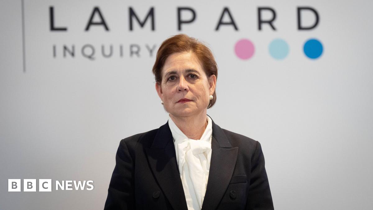 Baroness Kate Lampard wears a black jacket over a white shirt. She stands in front of a white background with the wording "Lampard Inquiry" in black letters, followed by three coloured dots.