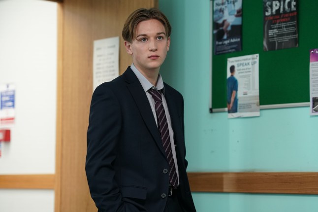 Joel Marshall standing in a meeting room in a suit and tie in EastEnders.