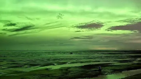Natalie Cherubini A vivid green light in the sky illuminates the seascape on a beach