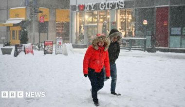 Two people, dressed in thick coats, walk through the snow in New York City