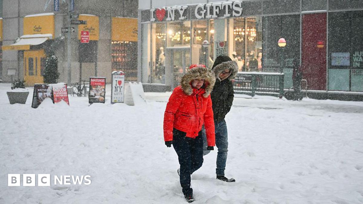 Two people, dressed in thick coats, walk through the snow in New York City