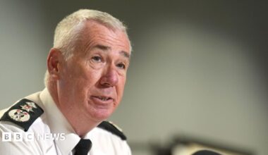 Jon Boutcher, a man with grey hair, wearing a white shirt, black tie and black and white lapels on his shouders.